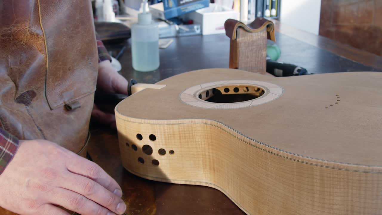 Liutaio al banco da lavoro che dimostra una giunzione a libro su una chitarra acustica.
