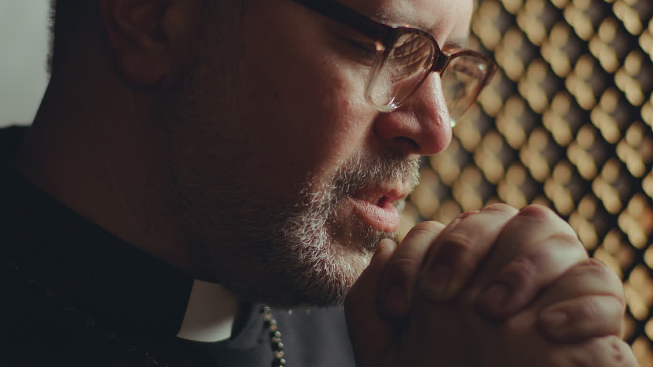 Close-Up of Priest Praying Deeply to God in Confessional