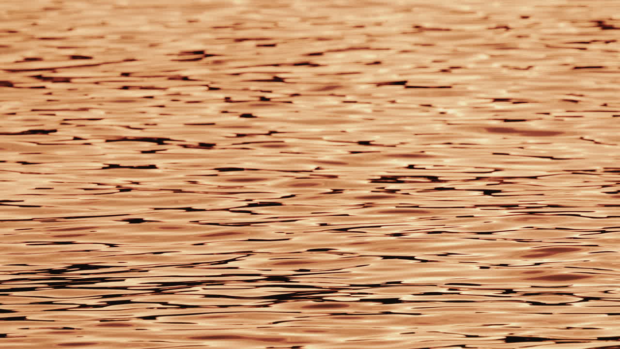 Close up of orange and gold sunset reflections moving across gentle water ripples