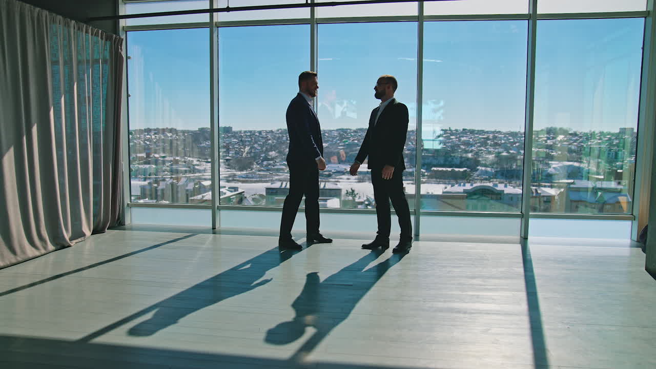 Meeting of businessmen indoors. Entrepreneurs in suits shaking hands in light office room against large panoramic windows with city view.