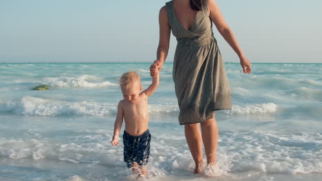 Glückliche-Mutter-Und-Kind,-Die-Am-Meeresufer-Aus-Dem-Wasser-Gehen.-Süßes-Kind,-Das-Im-Wasser-Sitzt.