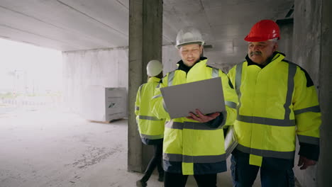 civil engineers are viewing construction plan in laptop and examining under-construction building