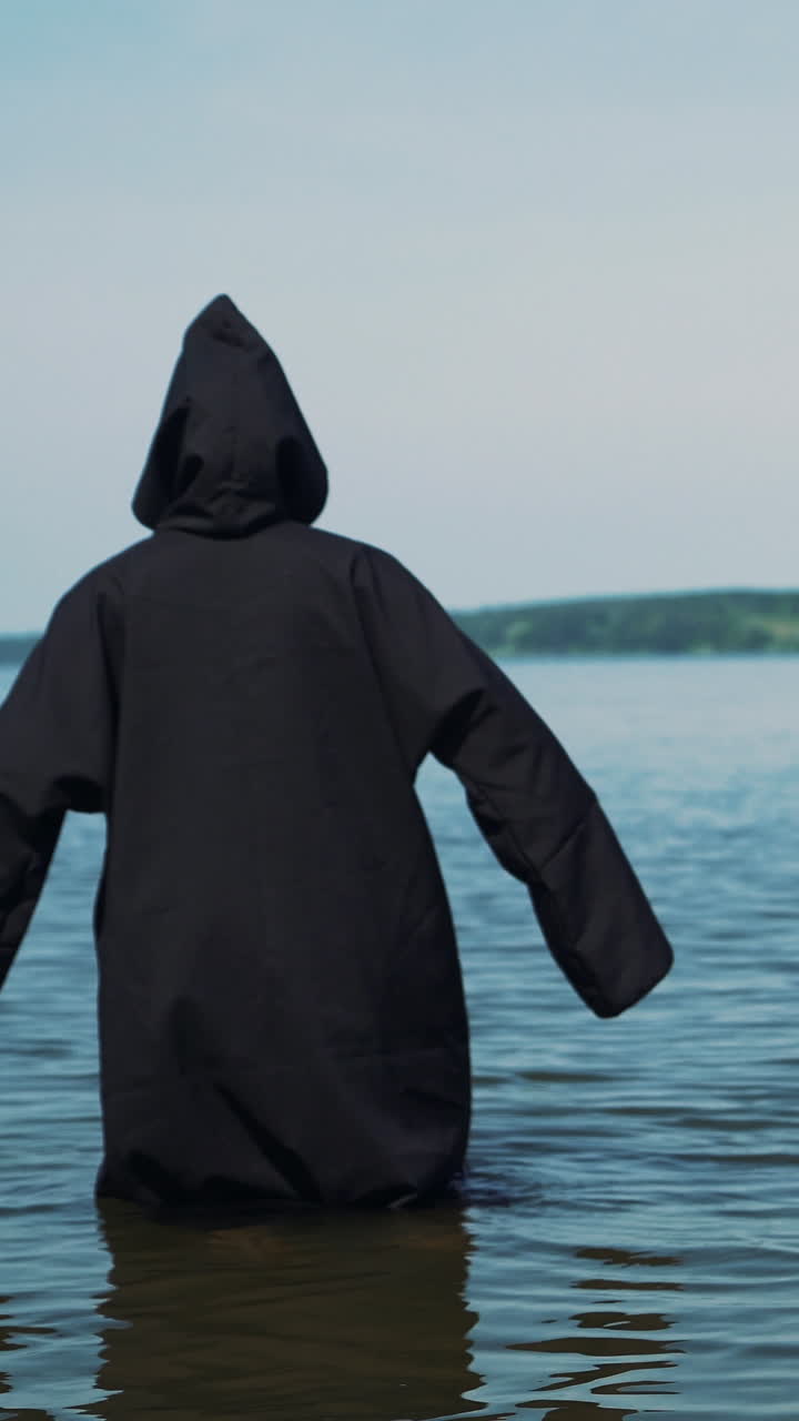Scary figure in black mantle in the river. Mysticism of Halloween. Halloween costume. Vertical video