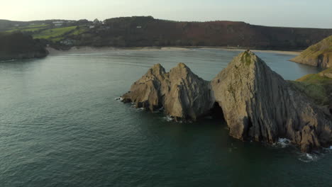 smooth drone aerial shot of three cliffs bay with couple on the cliff in the gower, wales, surrounded by the sea