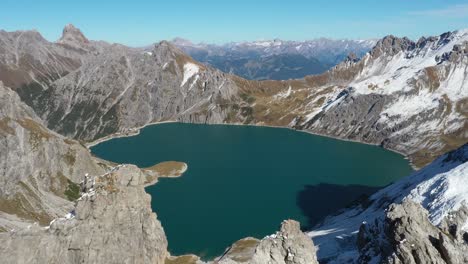 a drone shot flying forward and over the sharp and pointy peaks on top of the mountain lunersee, revealing the heart shaped lake love heart