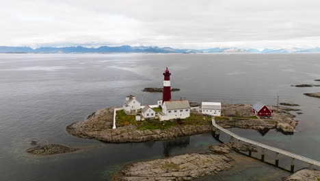 Un-Puente-Viejo-Y-Delgado-Conduce-Al-Faro-Solitario-En-La-Isla-Tranoy-Con-Vistas-A-Las-Montañas