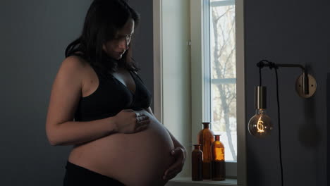 Heavily-pregnant-brunette-woman-looks-down-at-baby-bump