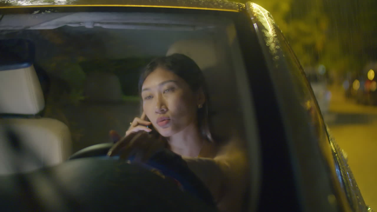 AsianWoman Speaking on Phone in Car under Pouring Rain