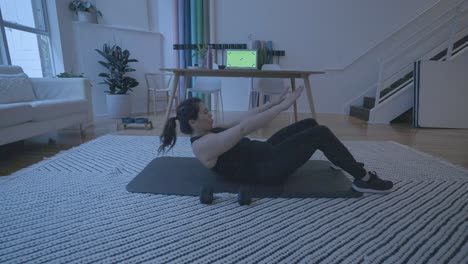 una mujer haciendo abdominales frente a una computadora con una pantalla verde mientras está en su casa en su sala de estar 4k60