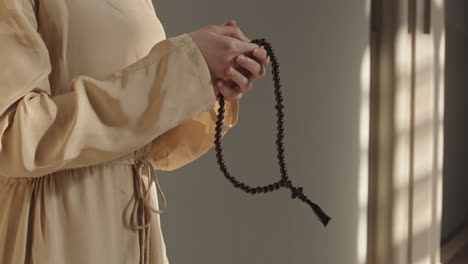 unrecognizable woman holding rosary beads and praying heartily