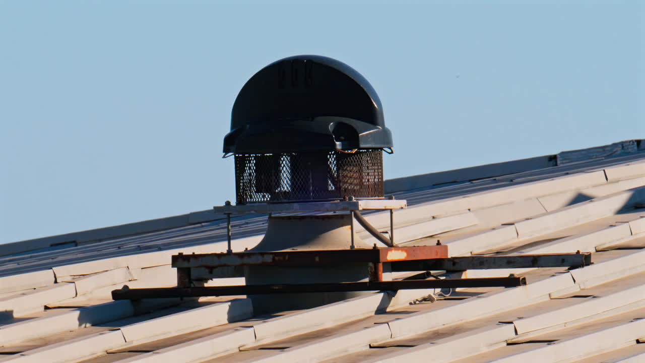 Close-up of a ventilation system mounted on a metal roof with the blue sky on the background