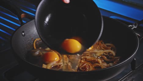 hinzufügen von eiern zu einer bratpfanne mit gebratenen zwiebeln darauf, nahaufnahme