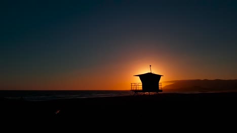 Slow-sideways-sunset-shot-at-San-Buenaventura-State-Beach-with-Lifeguard-house-:-tower-in-Ventura,-California,-United-States