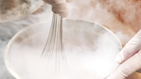 장갑을 입은 남성 요리사 손이 휘파람과 액체 질소를 사용하여 베리와 과일에서 맛있는 아이스크림을 준비하는 클로즈업