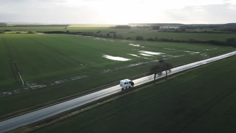 Vista-Aérea-De-Drones-De-La-Carretera-De-Conducción-De-Autocaravanas-Entre-Campos-Verdes,-Paisaje-Plano,-Día-Soleado-Después-De-La-Lluvia