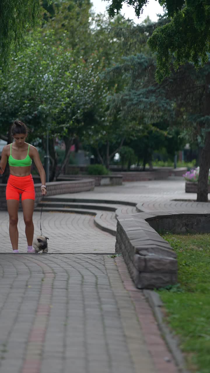 una mujer caminando con su pug en un parque.
