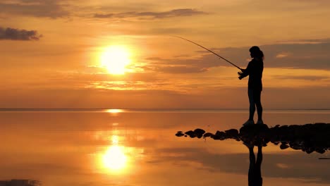 frau fischt auf einer angelstange, die sich im hintergrund beim sonnenuntergang dreht.