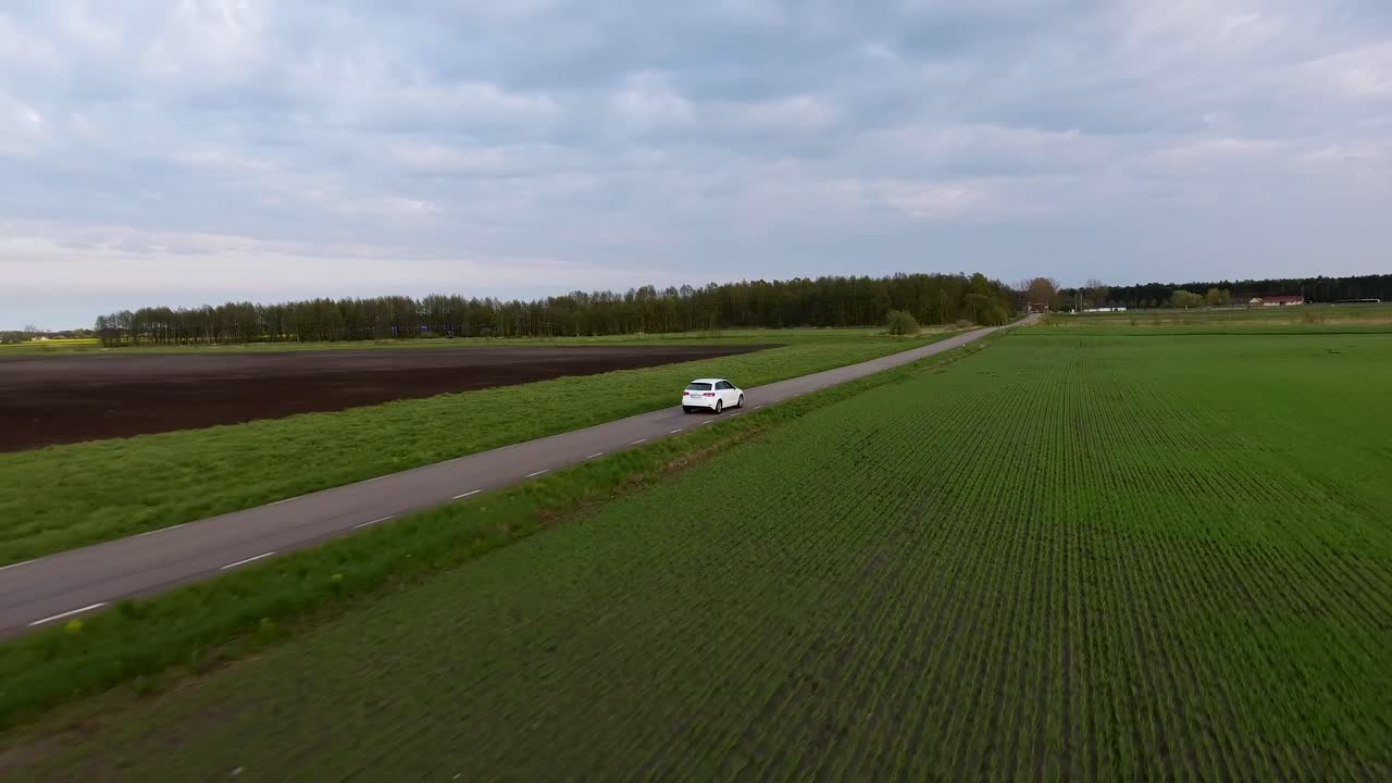 Aerial Drone Following Shot of a White car Driving on a Narrow Country side Road in South Sweden Skåne