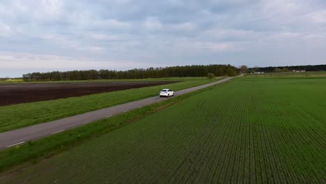 aerial drone following shot of a white car driving on a narrow country side road in south sweden skåne