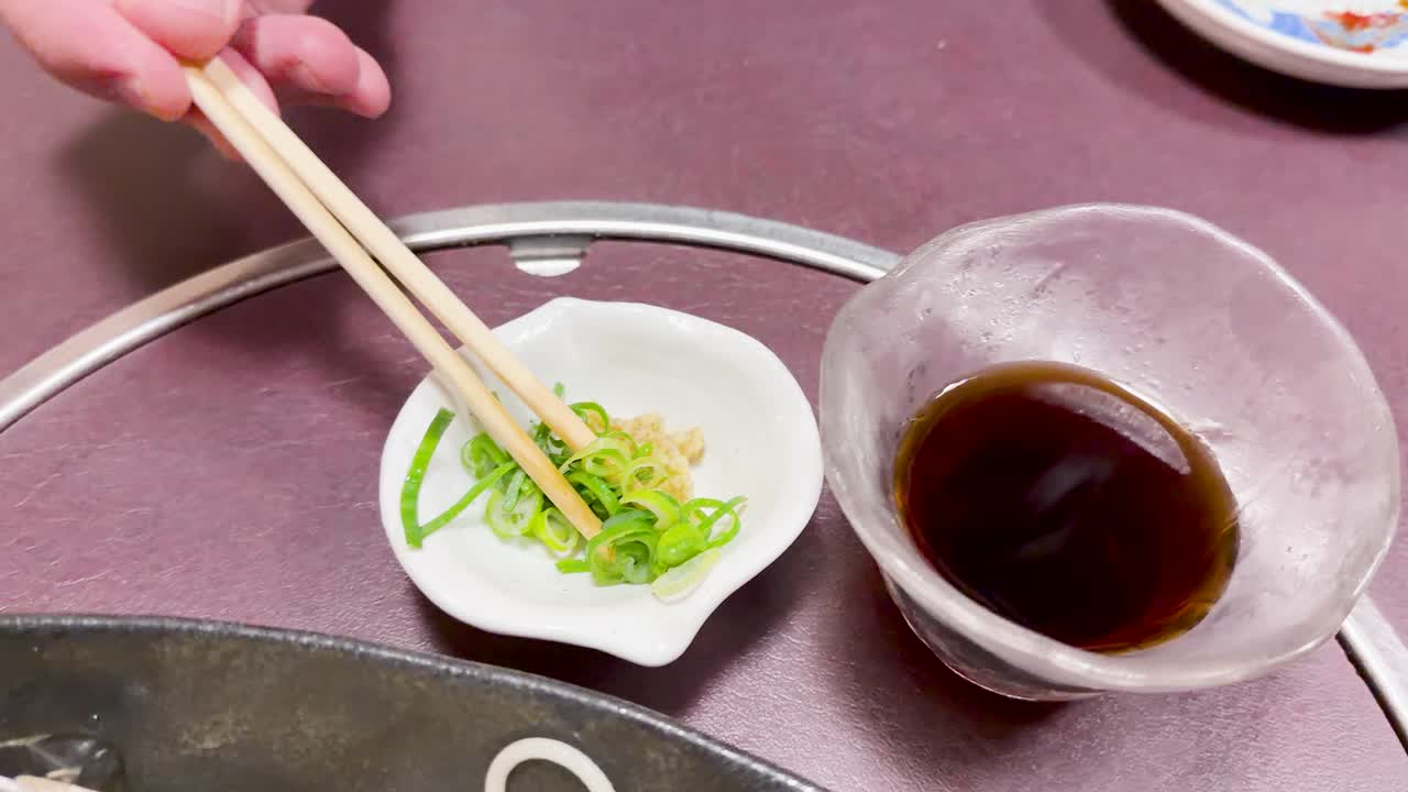 Bacchette prendono cipollotti verdi e li intingono nella salsa tsuyu accanto a noodle somen freddi