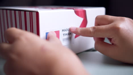 Hands-applying-MADE-IN-TIWAN-flag-label-on-a-shipping-cardboard-box-with-products