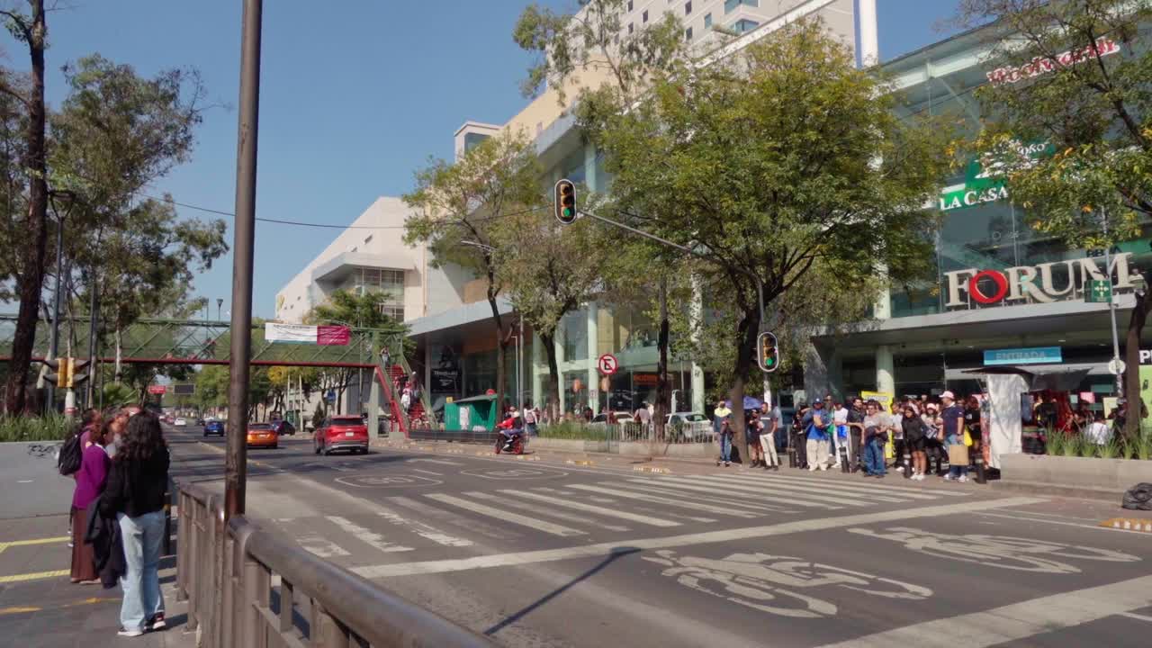 Busy city intersection with cars, pedestrians, and a shopping center on a sunny day