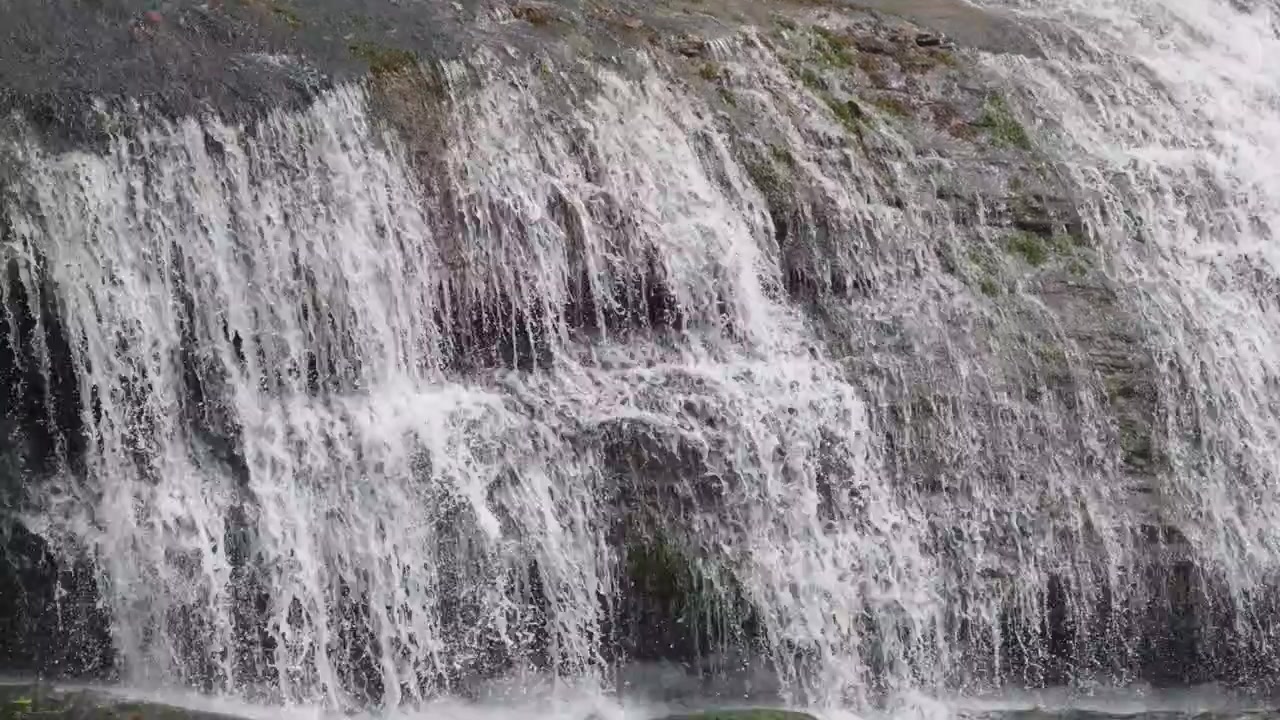 water cascade in Munnar, Kerala, with clear white water flowing rapidly over a rocky mountain slope, creating multiple layers of cascading waterfalls. The close-up view focuses on the powerful flow