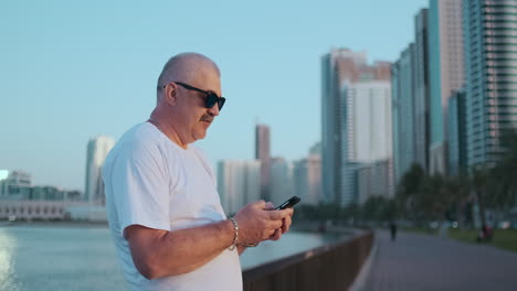 Bearded-senior-man-standing-outdoors-using-smartphone.-Retired-male-reading-news-chatting-with-his-children-via-mobile-phone.-Studying-city-map-app.-Lost-in-city-looking-for-right-direction.