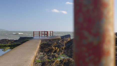 Concrete-pier-on-rocky-coastline-at-Portmarnock-beach,-Dublin,-Ireland-with-waves-crashing-in-winter