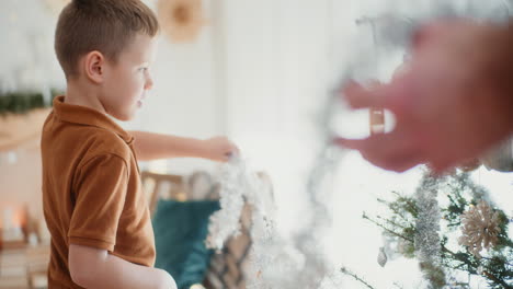 young boy hangs christmas tree chain on christmas tree and decorates it