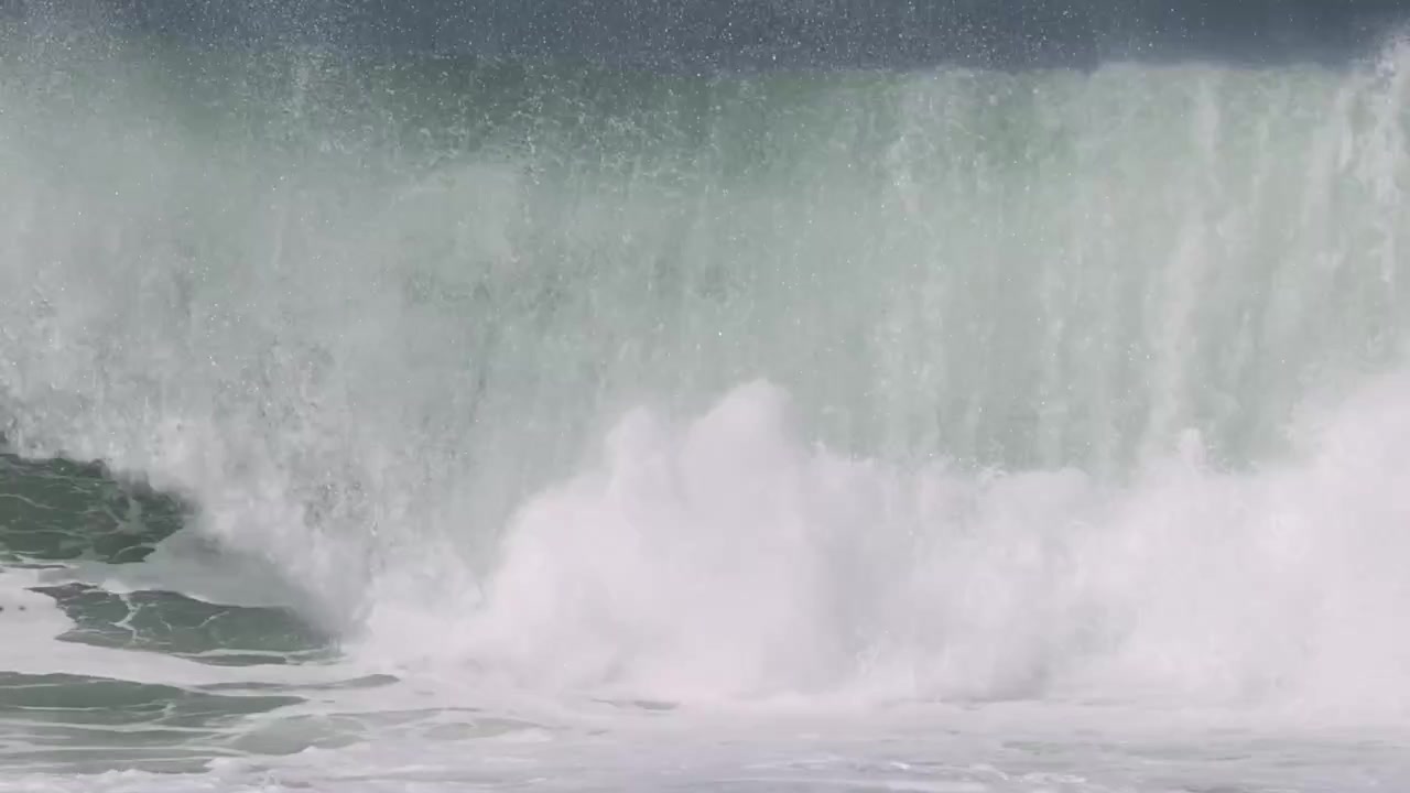A dynamic close-up shot of a large turquoise wave breaking into explosive white sea foam.