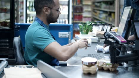 serious african american cashier scanning goods at checkout