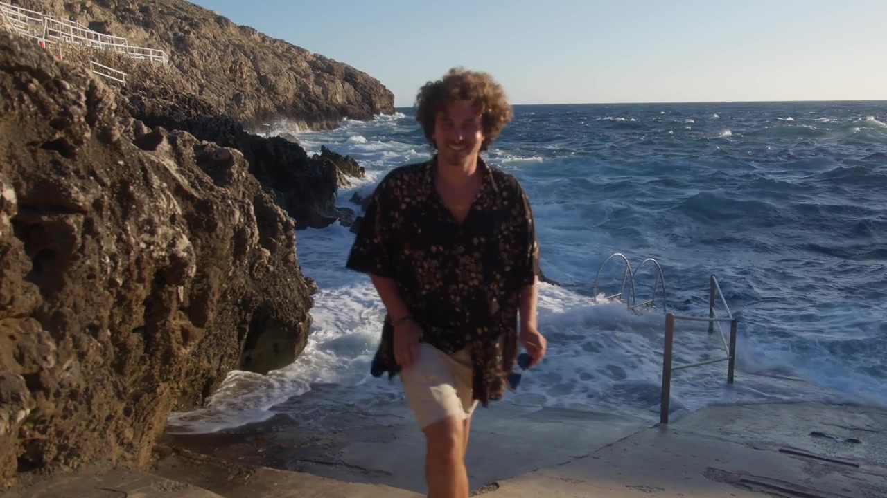 Un'inquadratura ampia di un uomo che ride e scappa dalle onde sulla spiaggia del Faro di Punta Carena, Isola di Capri