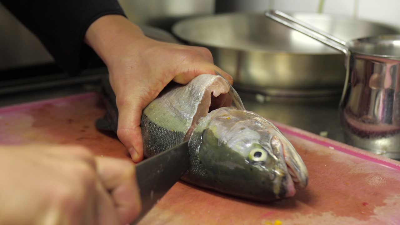 Chef cortando la cabeza de una trucha marmorata con un cuchillo grande en una tabla de cortar