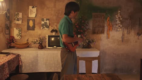 young asian male playing a guitar while walking around a rustic room