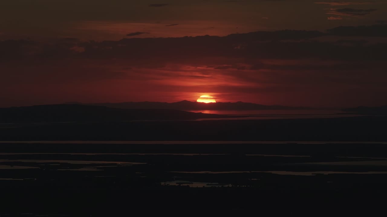 Drone close up shot from Bountiful Canyon in Utah of the sun setting below the Salt Lake Valley with clouds, mountains, and water ponds reflecting light from the Great Salt Lake
