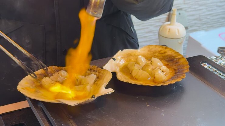 Close-up shot of a chef using a blowtorch to grill scallops in their shells