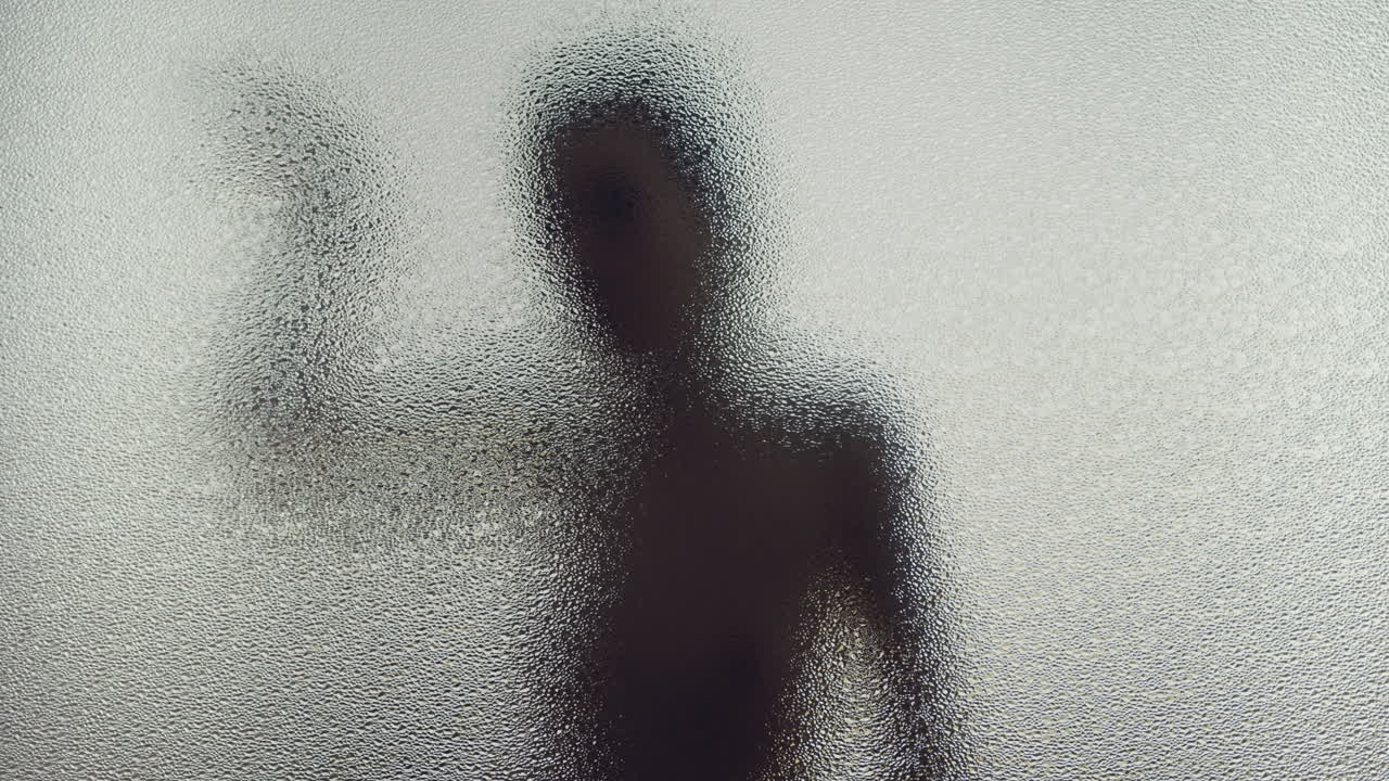 A female silhouette behind the frosted window dances slowly