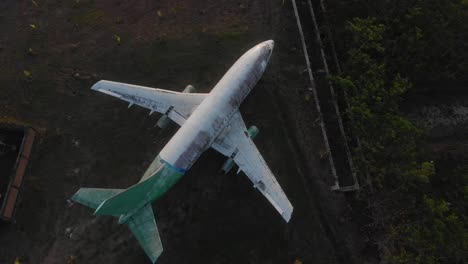 Top-down-view-of-abandoned-rusty-plane-on-meadow-at-Indonesia,-aerial