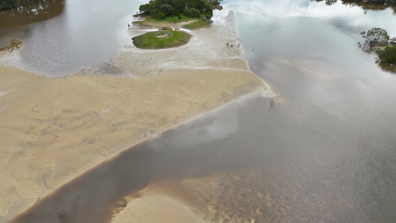 Drone captures river water breaching sandbar, flowing into ocean under soft daylight, wide perspective