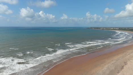 Vista-Aérea-Hacia-Atrás-De-Una-Gran-Bahía-De-Arena-Donde-Las-Olas-Blancas-Y-Espumosas-Llegan-A-La-Orilla