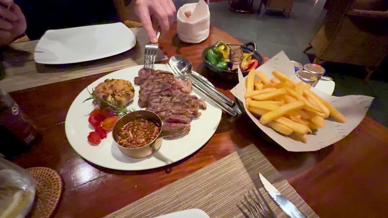 Una persona usa una forchetta per mangiare una bistecca alla griglia servita con patatine fritte a Phuket.