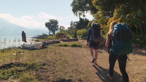 a couple of backpackers walk on the shores of lake atitlan, guatemala, with a volcano visible in the back