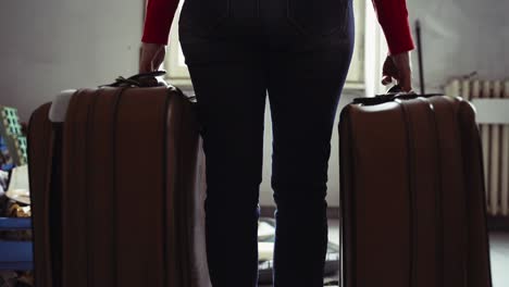 woman staying in empty room and holding two vintage travelling suitcases in her hands. sad woman leaving her sweet home, moving to new apartment, nostalgia concept. abandoned room with a pile of used things