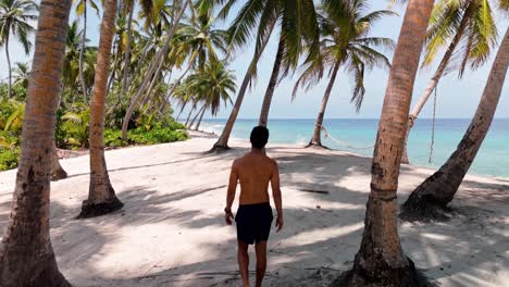 a solitary figure strolls barefoot along the curve of geiymiskih fannu beach, fuvahmulah, as gentle waves lap the crystal-clear shoreline.