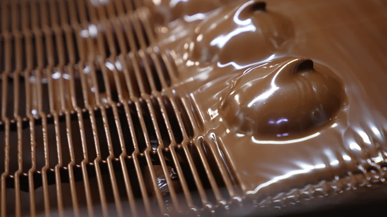 Thick layer of milk chocolate over the marshmallow desserts. Freshly-covered sweets move along the conveyor. Close up.