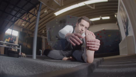 focused young sportsman doing warmup exercises and stretching legs in a bouldering gym 3