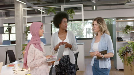 happy diverse creative female colleagues in discussion using laptop in office, slow motion