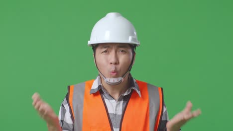close up of wondering asian male engineer with safety helmet saying why working doubtfully in the green screen background studio