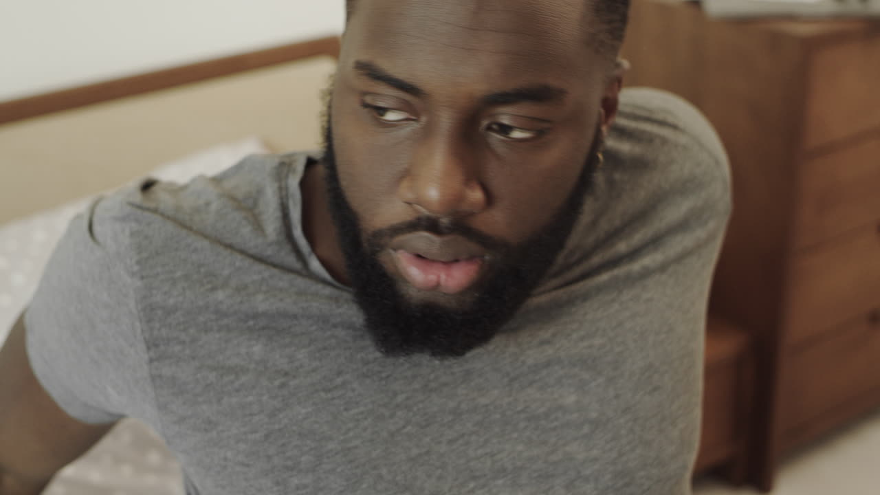 Black man waking up in morning fast. Black guy has hangover at bedroom.